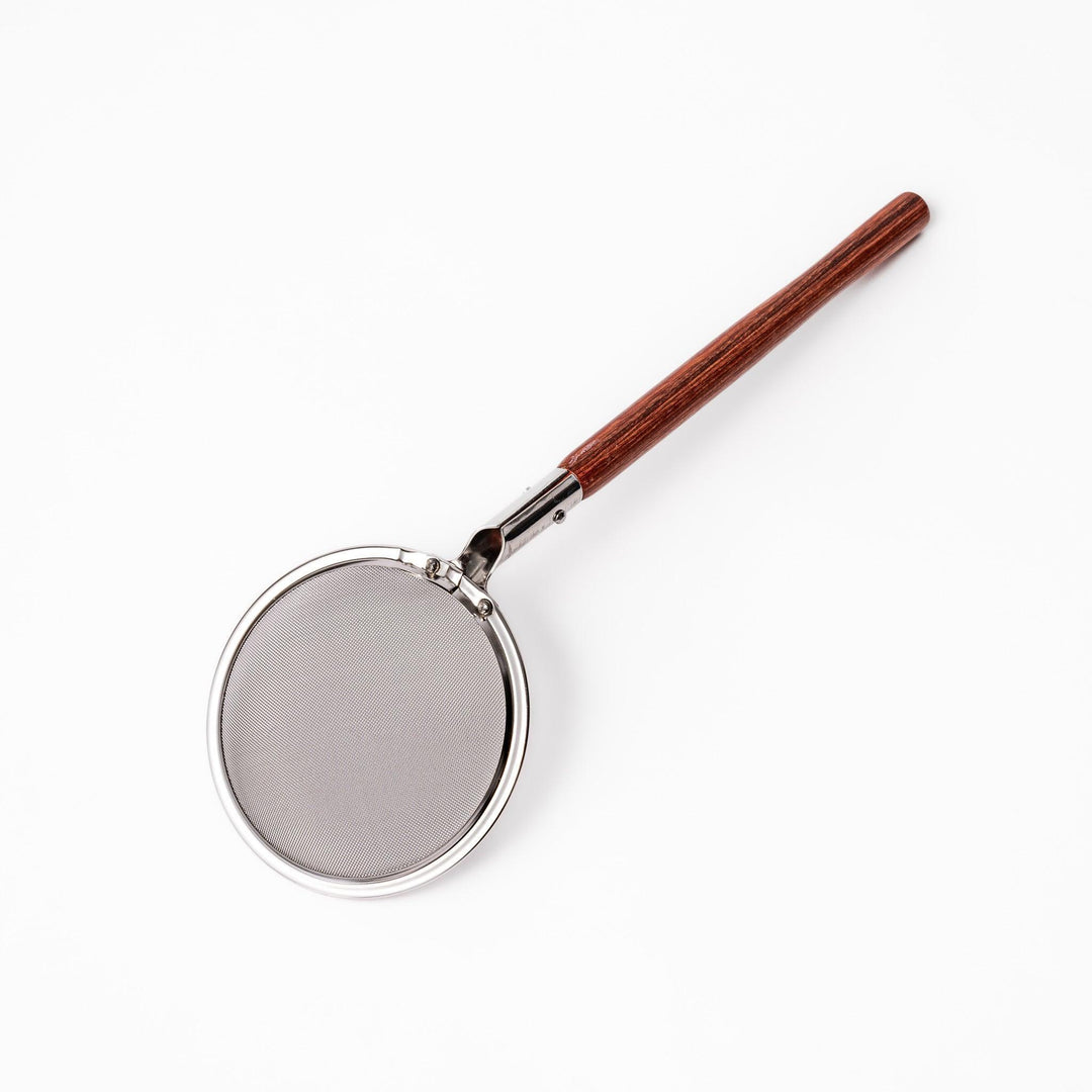 Stainless steel round-mesh skimmer with long wooden handle, perfect for straining soups and frying in home kitchens.