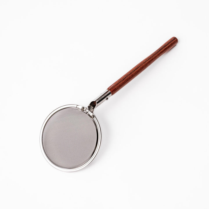 Stainless steel round-mesh skimmer with long wooden handle, perfect for straining soups and frying in home kitchens.
