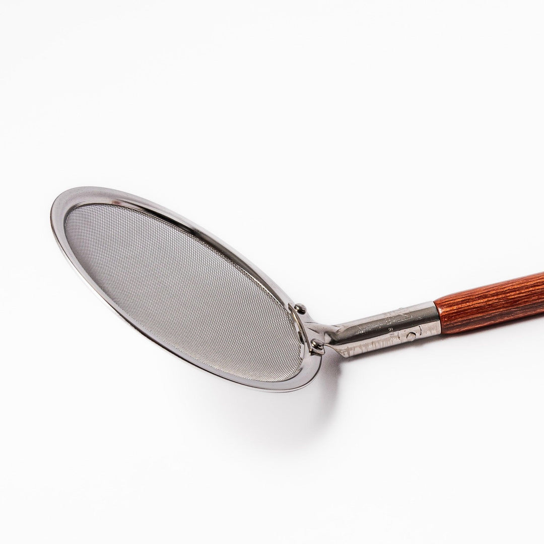 Stainless steel round-mesh skimmer with long wooden handle, perfect for straining soups and frying in home kitchens.