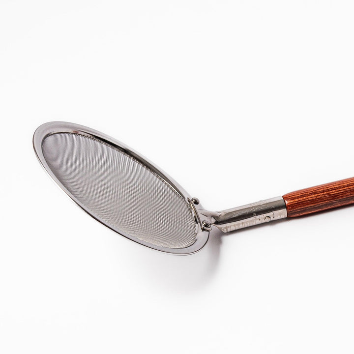 Stainless steel round-mesh skimmer with long wooden handle, perfect for straining soups and frying in home kitchens.