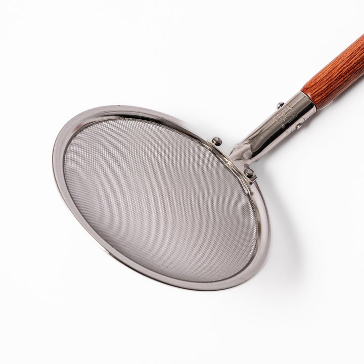 Stainless steel round-mesh skimmer with long wooden handle, perfect for straining soups and frying in home kitchens.