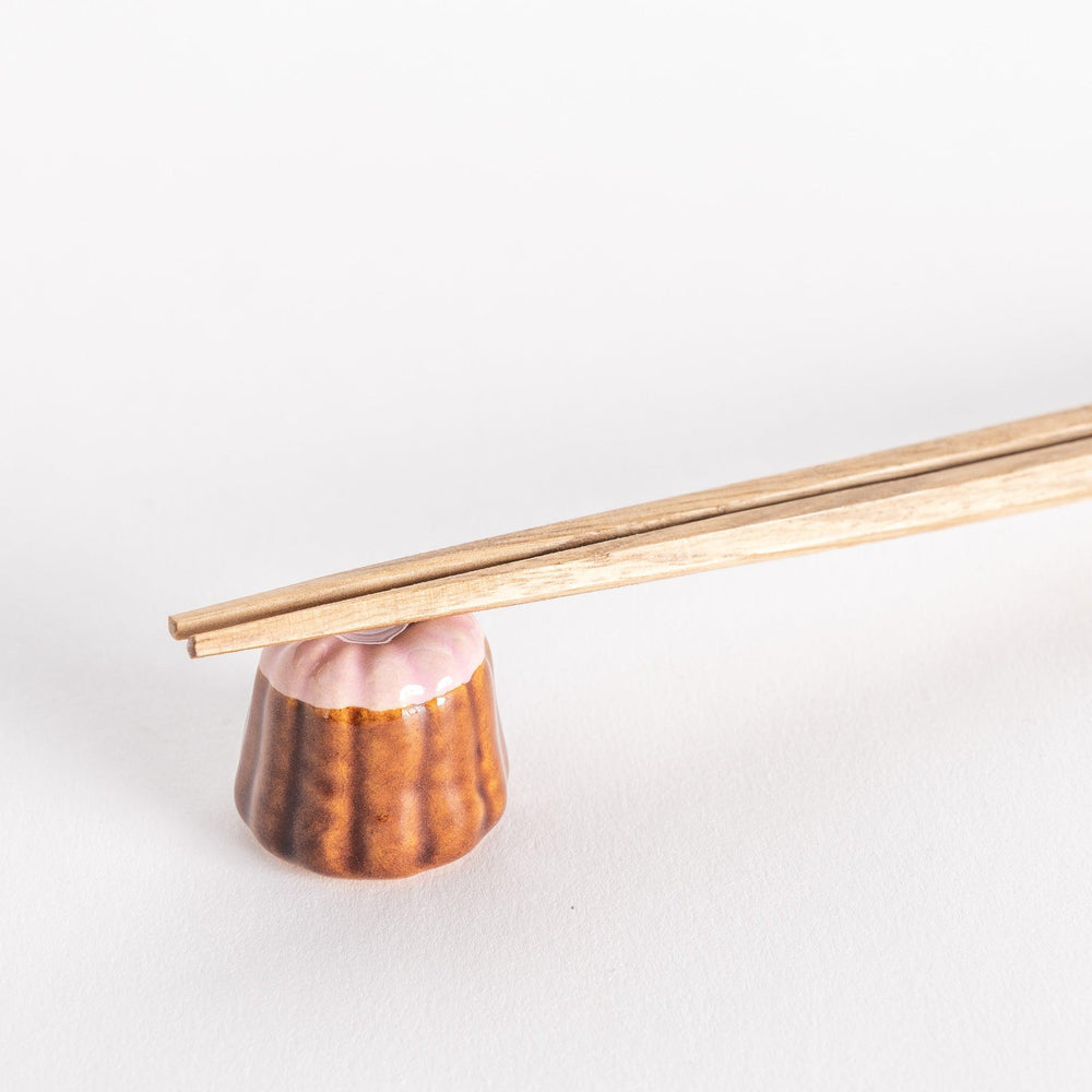 Strawberry canelé shaped ceramic chopstick rest with pink top and brown ridged base for cute look.