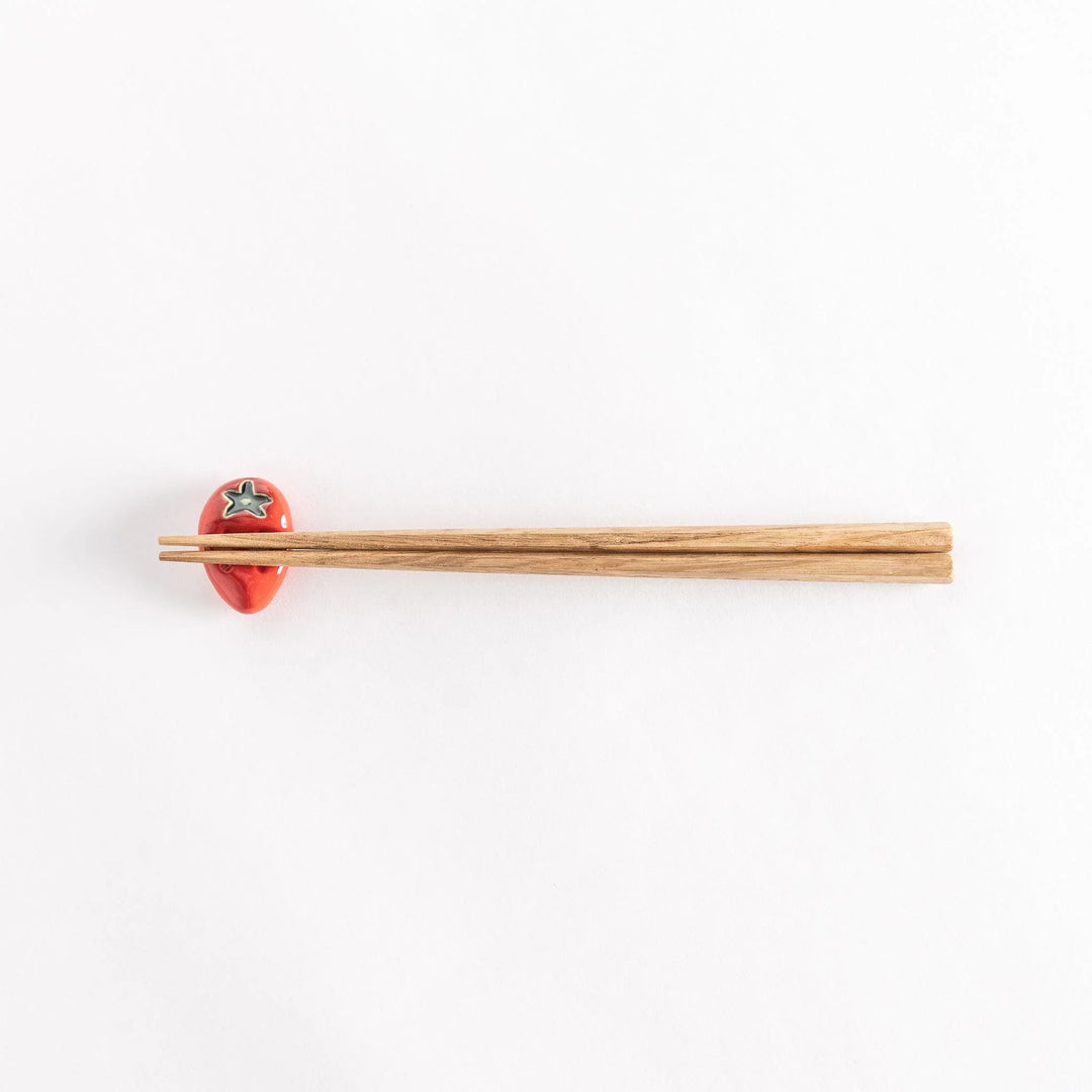 The strawberry chopsticks rest with chopsticks resting across, showcasing its realistic strawberry design.