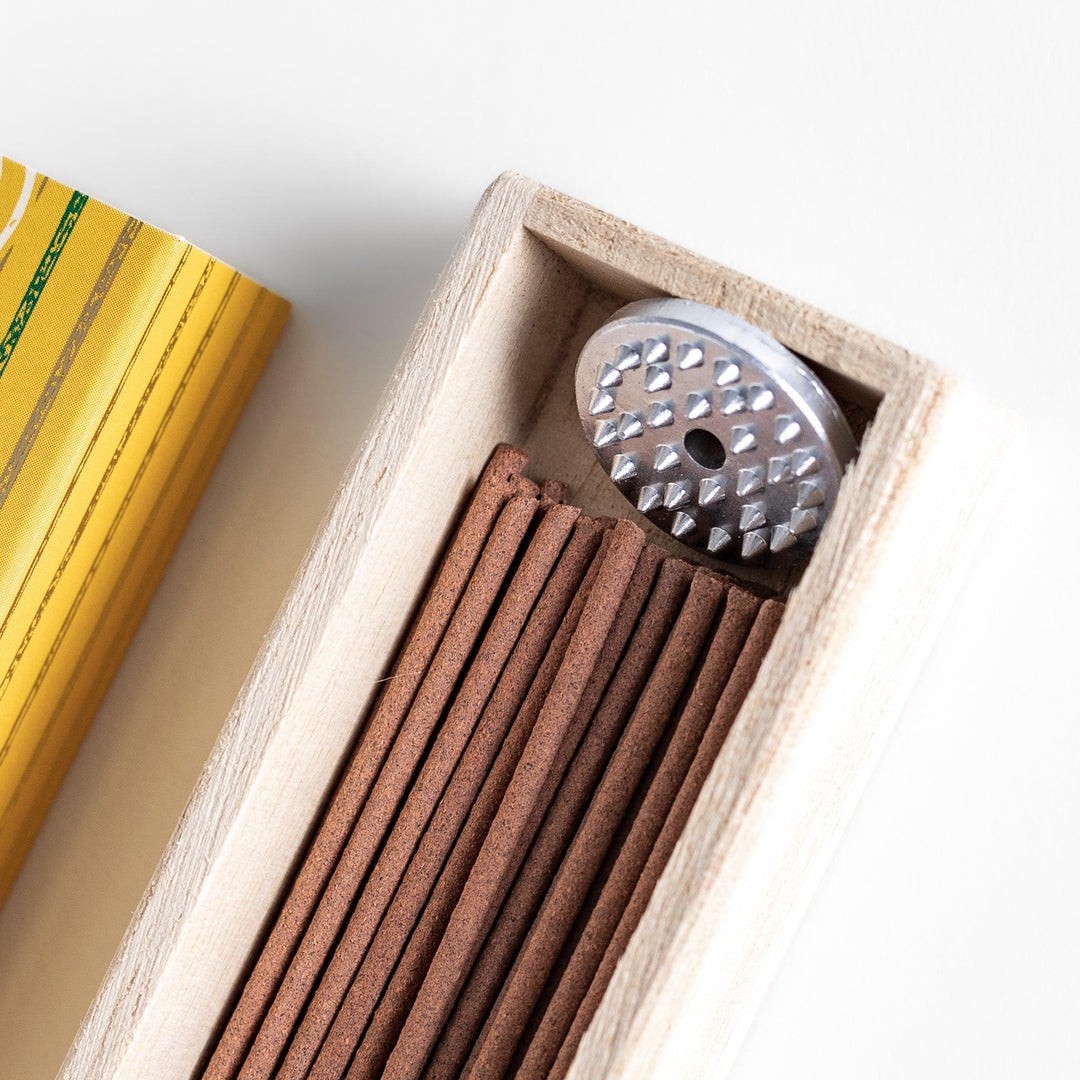 Japanese incense in wooden box with brown sticks and yellow design featuring white circle patterns.