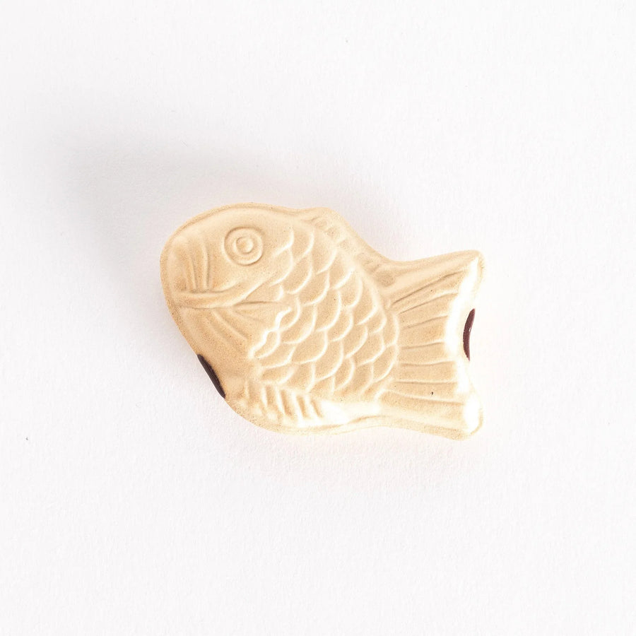 A ceramic chopsticks rest shaped like a taiyaki fish, featuring detailed scales and fins in a soft beige color.