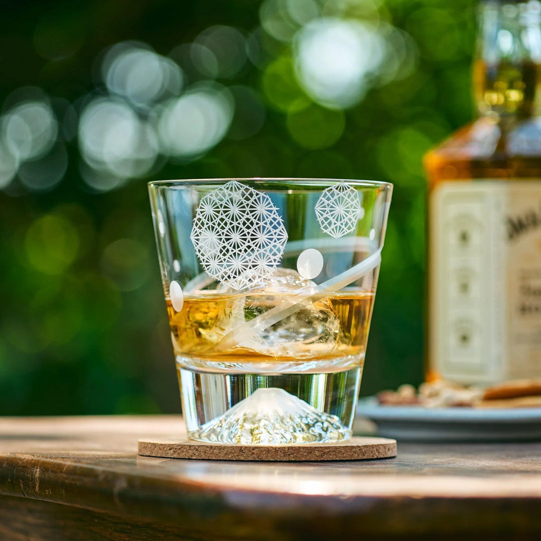 Japanese whiskey glass with Mt. Fuji base and traditional Asanoha patterns, filled with whiskey and ice outdoors.