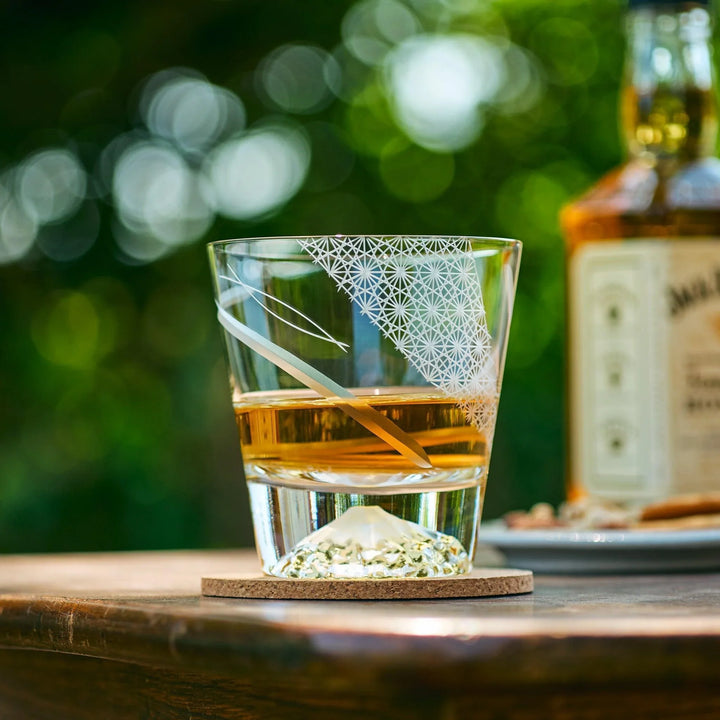 Japanese Kiriko whiskey glass with Mt. Fuji base and slanted Asanoha patterns, filled with whiskey and ice outdoors.
