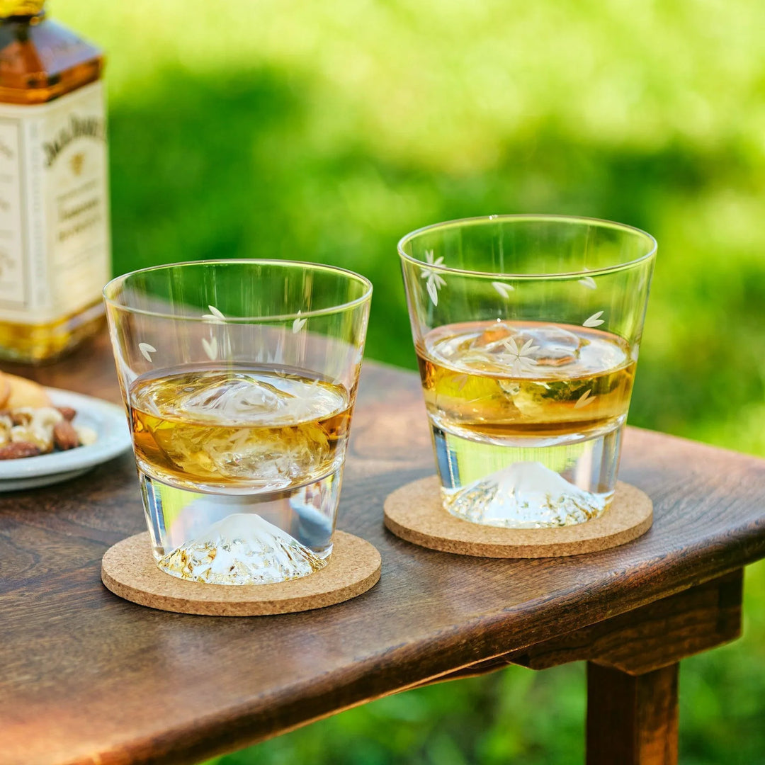 Japanese whiskey glasses with Mt. Fuji bases and sakura engravings, filled with whiskey on a table.
