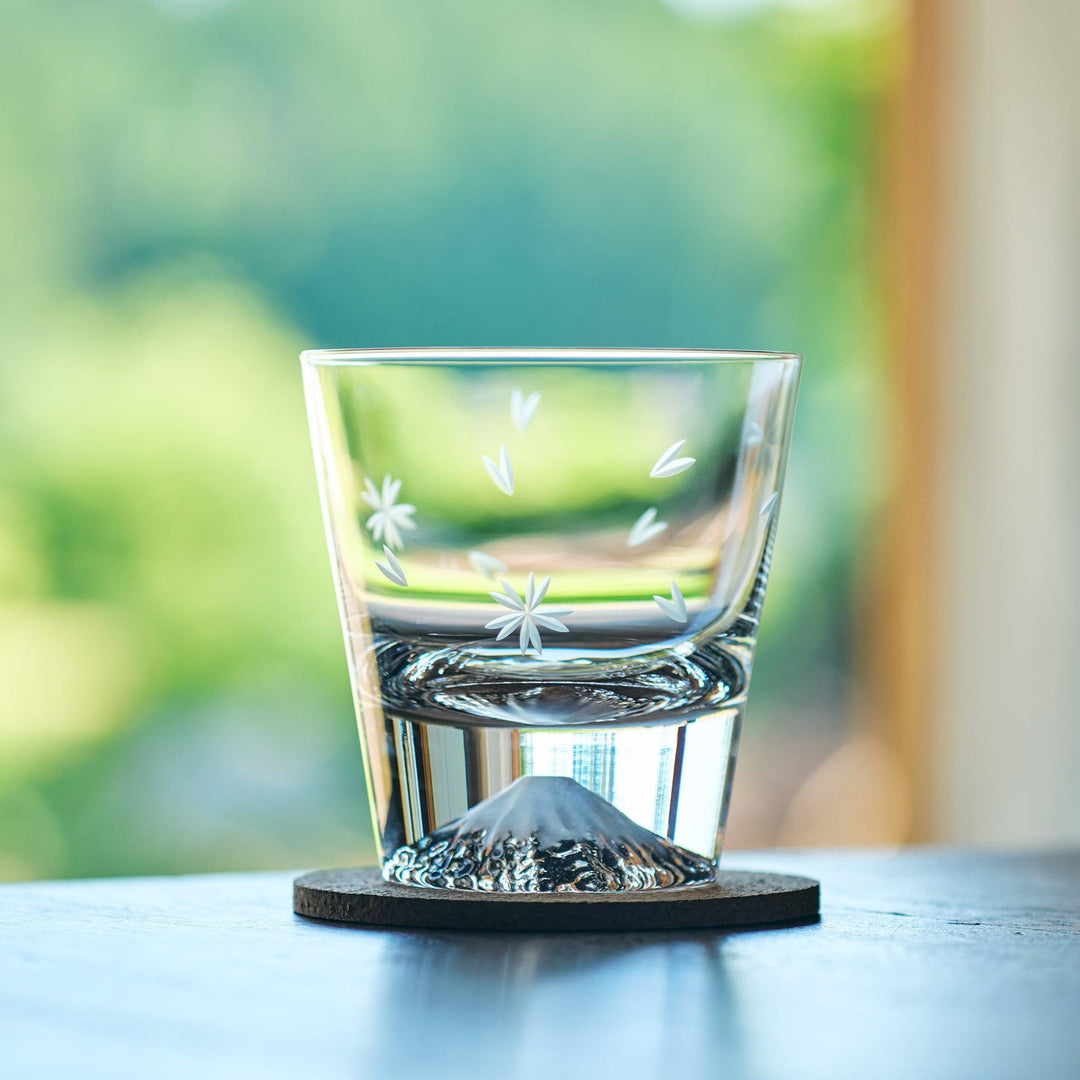 Clear Japanese glass with sakura engravings and a Mt. Fuji-shaped bottom, resting on a cork coaster.