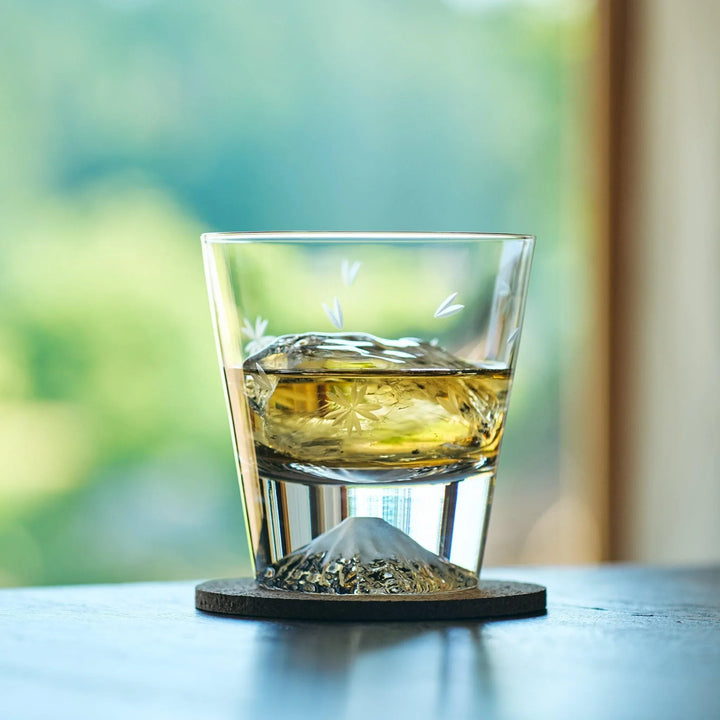 A Japanese whiskey glass with Mt. Fuji-shaped base and sakura engraving, filled with whiskey and ice.