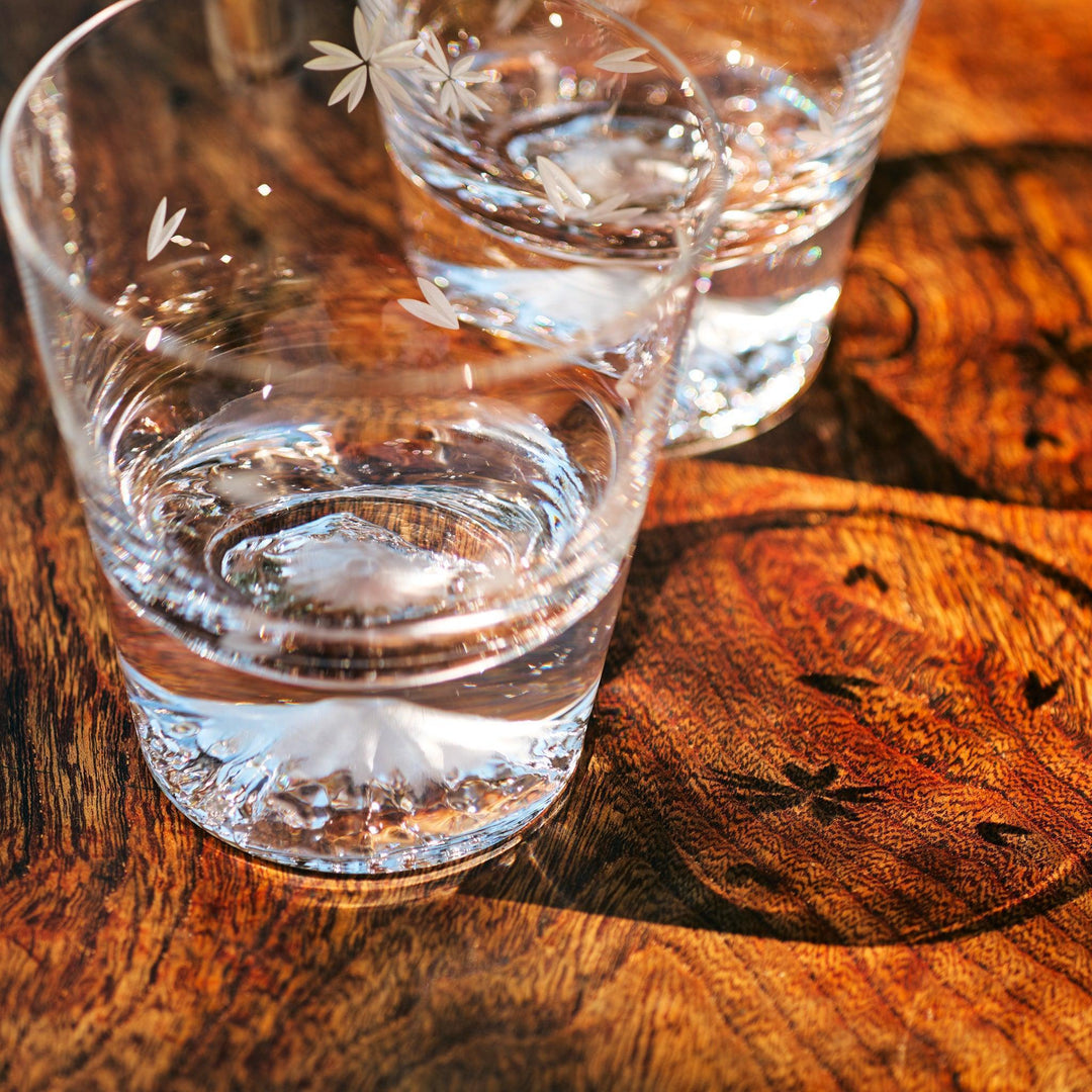 Close-up of Mt. Fuji-base Japanese glasses with sakura engravings, casting shadows on a wooden table.
