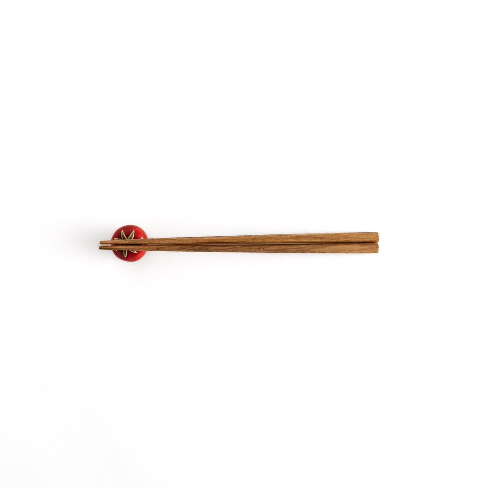 Wooden chopsticks balanced on the glossy red tomato chopstick rest, showcasing its functional and decorative design.