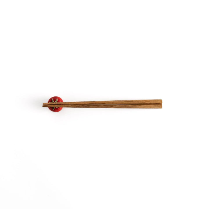 Wooden chopsticks balanced on the glossy red tomato chopstick rest, showcasing its functional and decorative design.