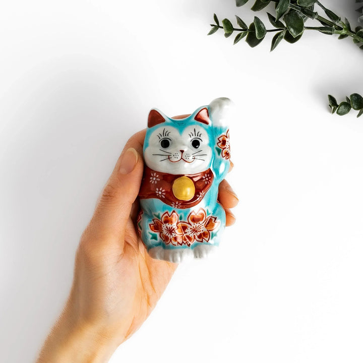 Turkish blue Japanese Maneki Neko figurine with floral patterns golden bell and raised paw for good fortune.
