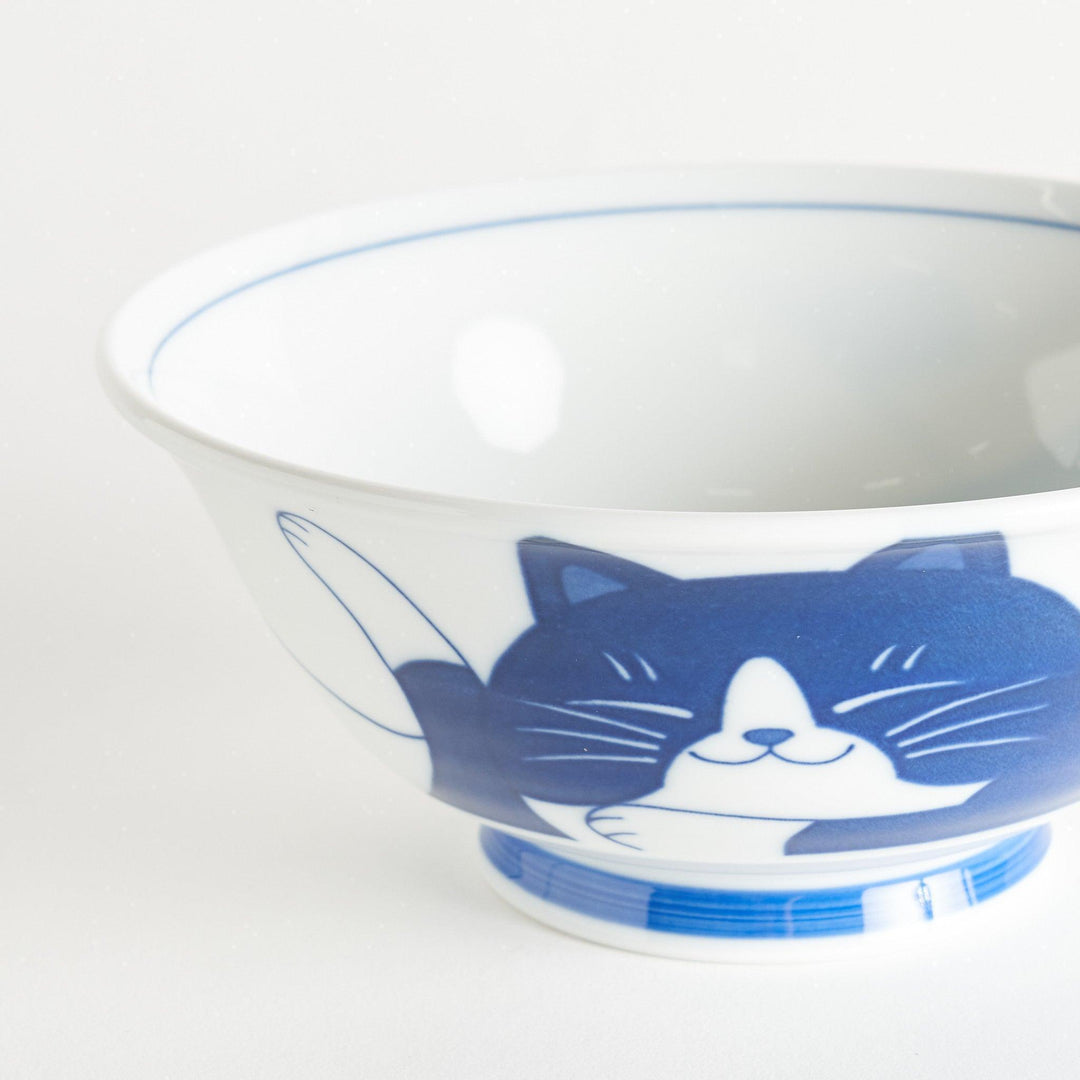 A white ramen bowl featuring a playful blue cat lying down with its eyes closed.