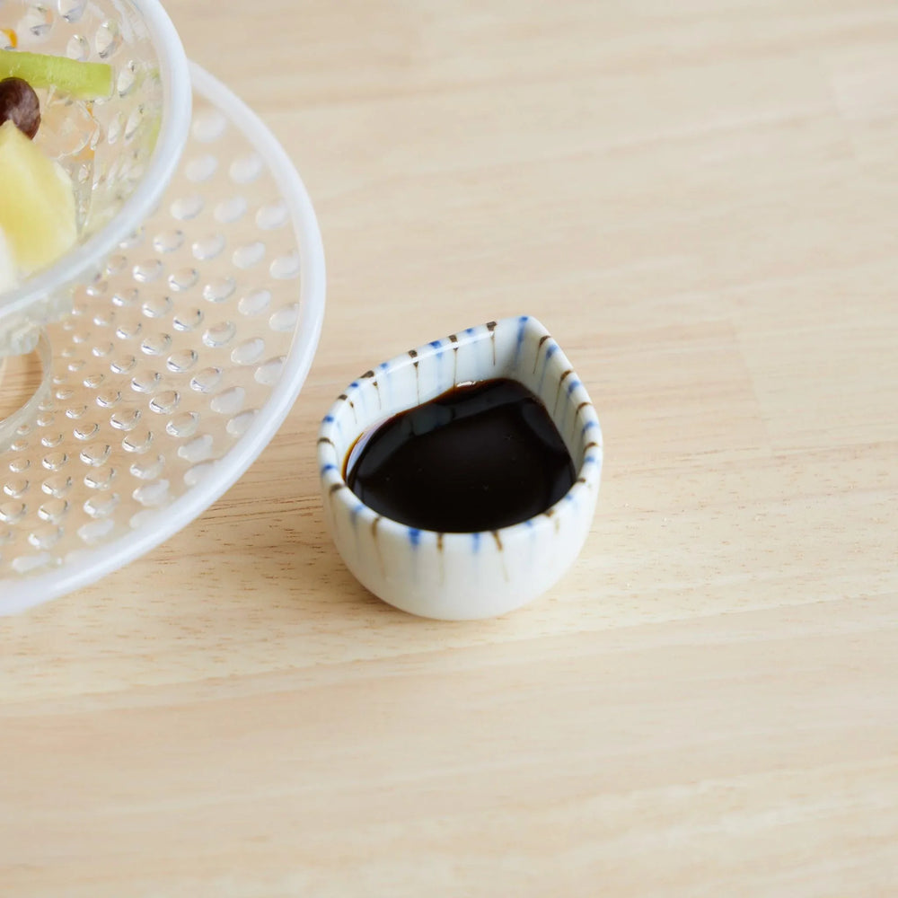 Small teardrop-shaped ceramic bowl with blue hand-painted lines, filled with kuromitsu syrup for anmitsu dessert.