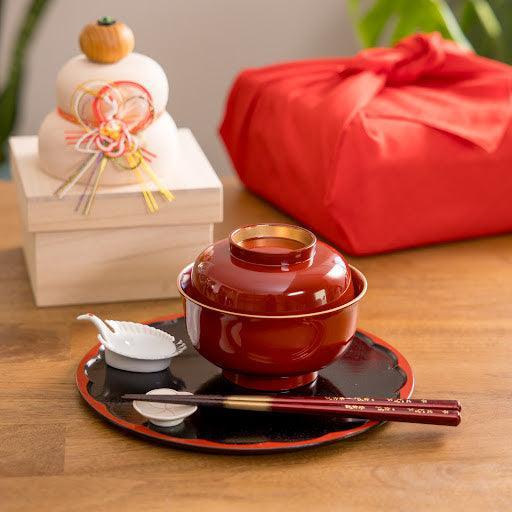 Vermilion lacquer miso soup bowl with lid on tray beside chopsticks and crane condiment dish.