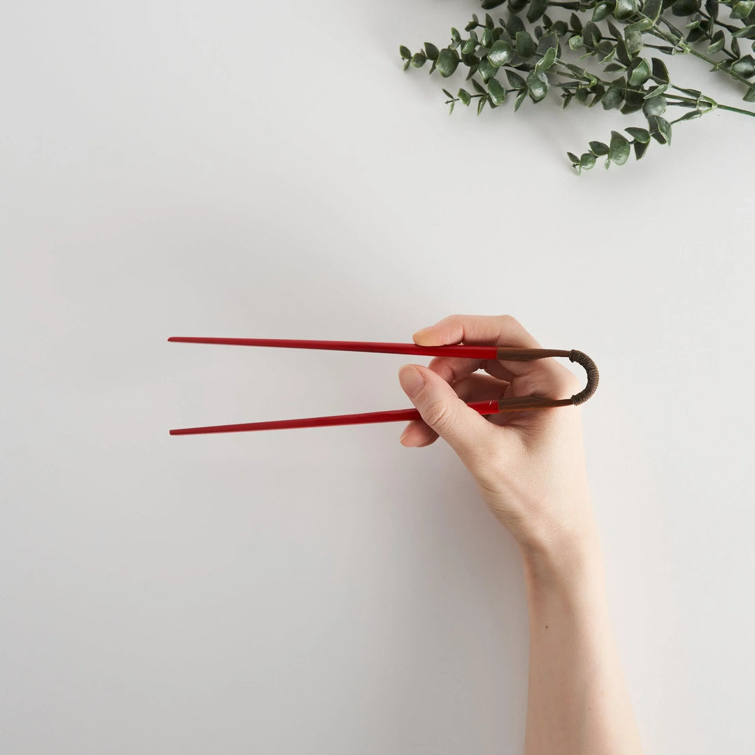 Hand holding red chopsticks with a wooden curved joint, displaying their sleek design and modern appeal.