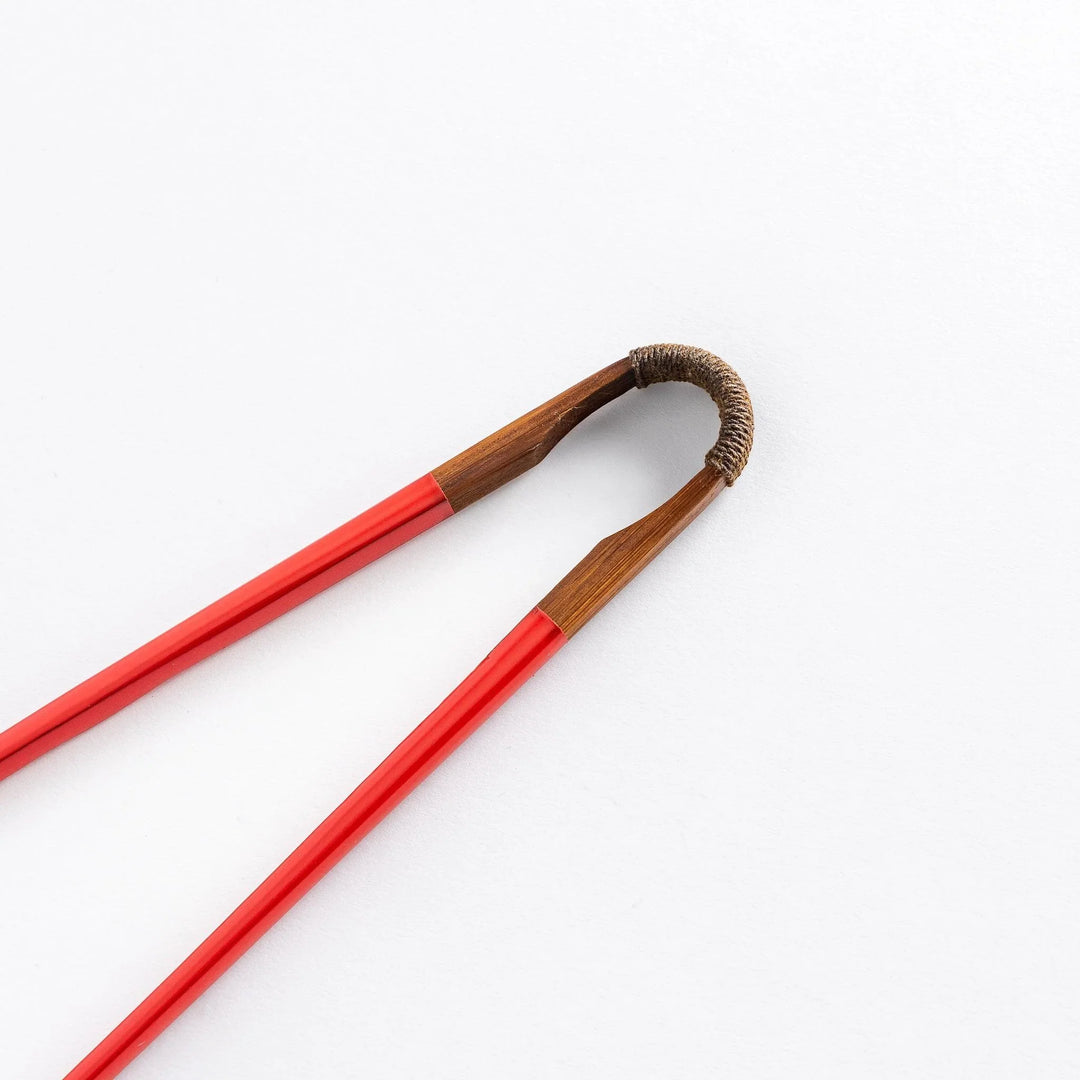 Red chopsticks with curved wooden joint showing natural wood connection and elegant Japanese craftsmanship.