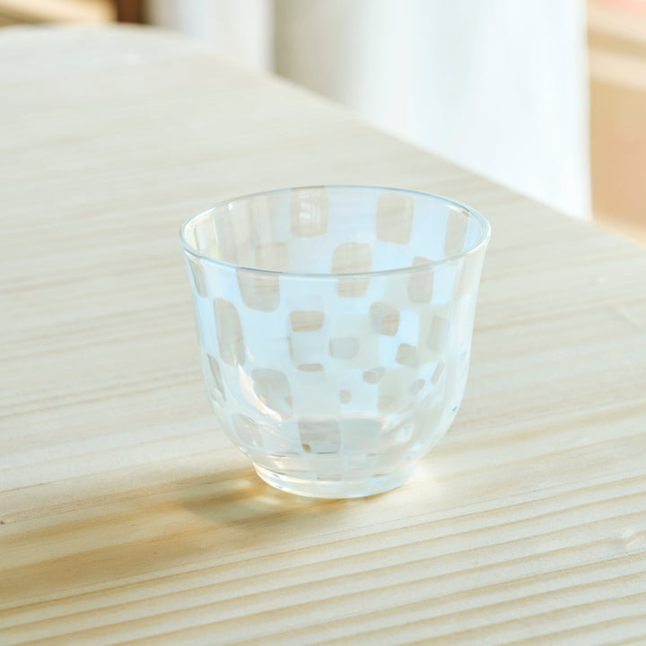 Vintage Japanese glass tea cup with white checkered patterns on a natural wooden table in bright morning sunlight