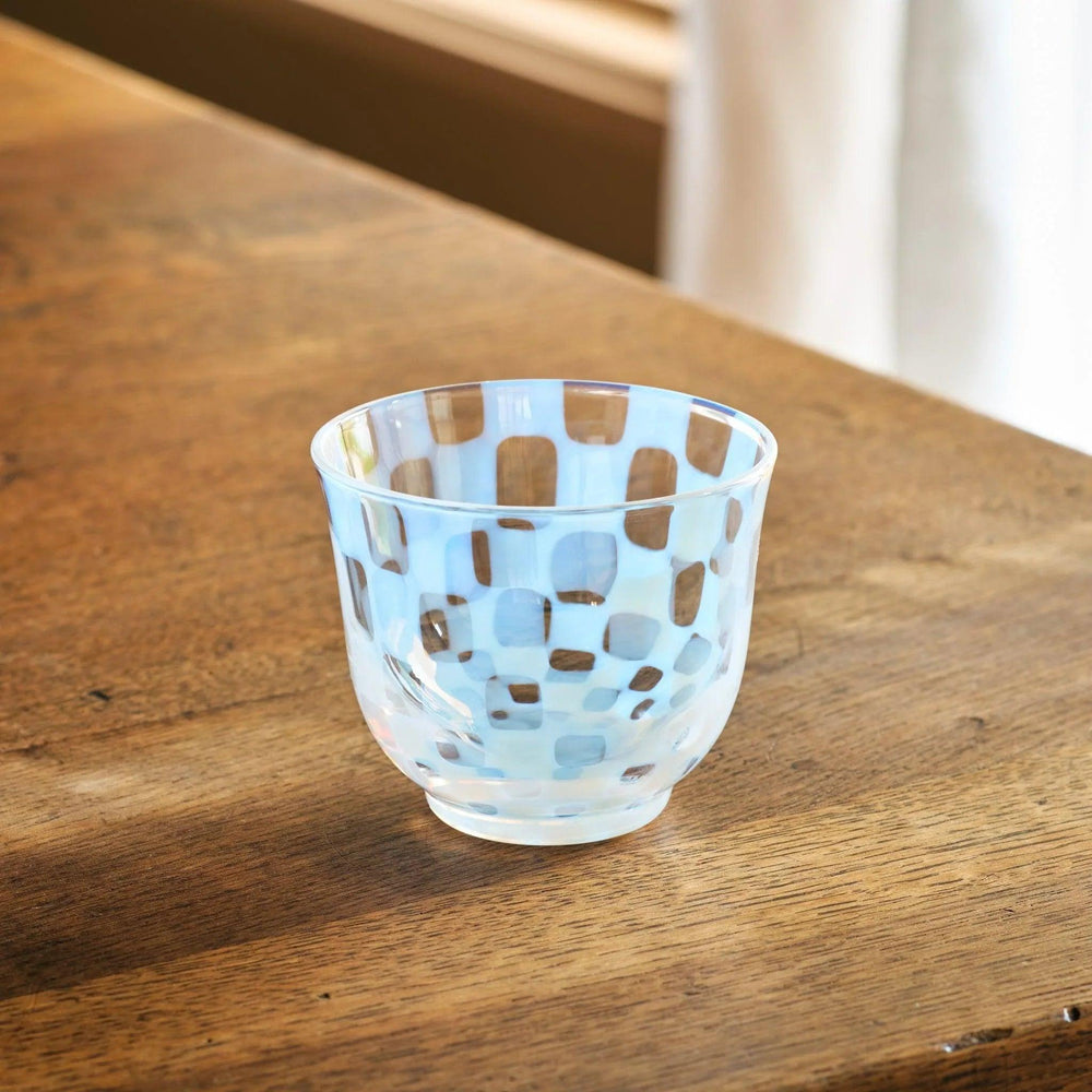 A vintage-style glass tea cup with a light blue checkerboard pattern, placed on a wooden table in natural light.