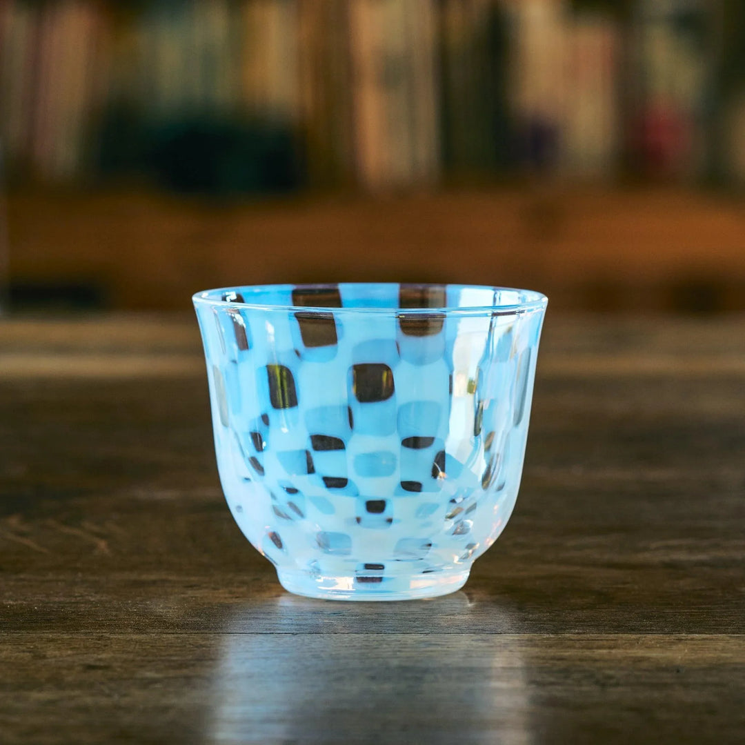 An empty glass tea cup with a blue and clear checkered pattern, resting on a wooden table with a soft background.