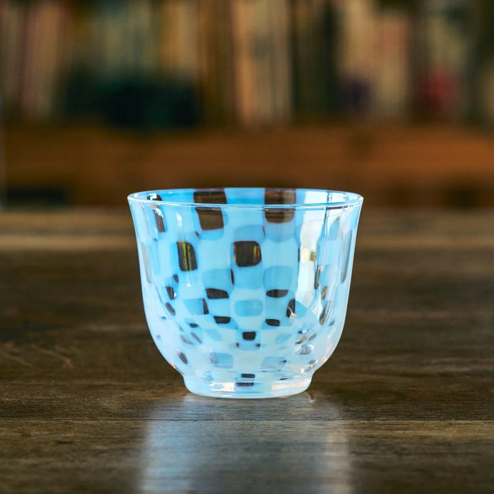 An empty glass tea cup with a blue and clear checkered pattern, resting on a wooden table with a soft background.