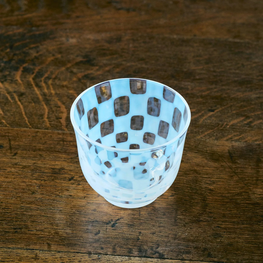 A Japanese glass tea cup with soft blue and clear checkered patterns, viewed from an overhead angle on wood.