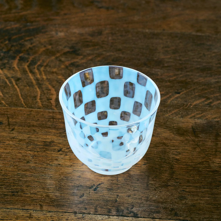 A Japanese glass tea cup with soft blue and clear checkered patterns, viewed from an overhead angle on wood.