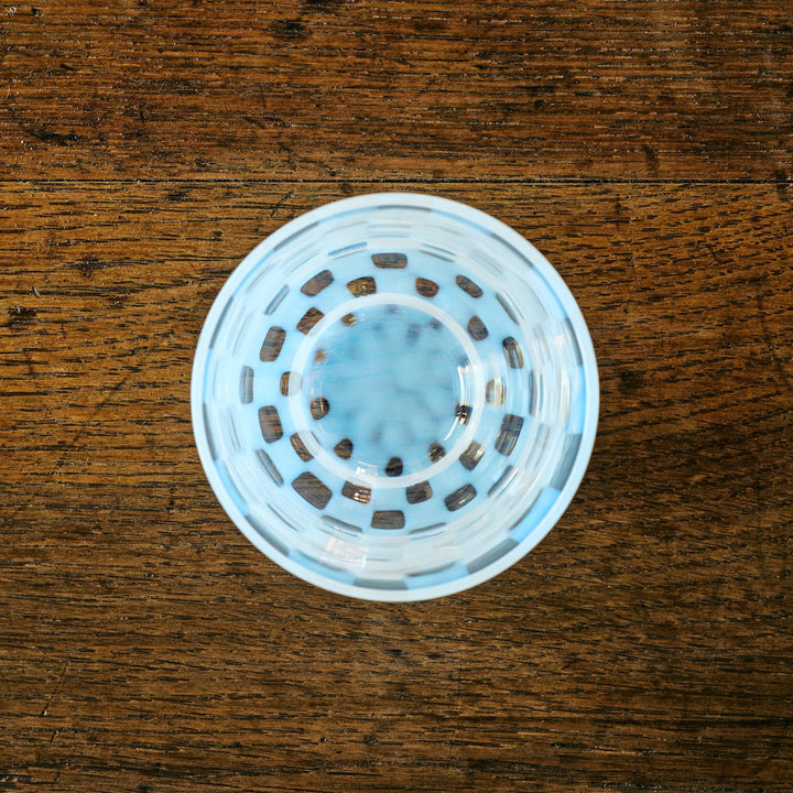 Top-down view of a glass tea cup featuring concentric checkered rings in pale blue, resting on a wooden table.