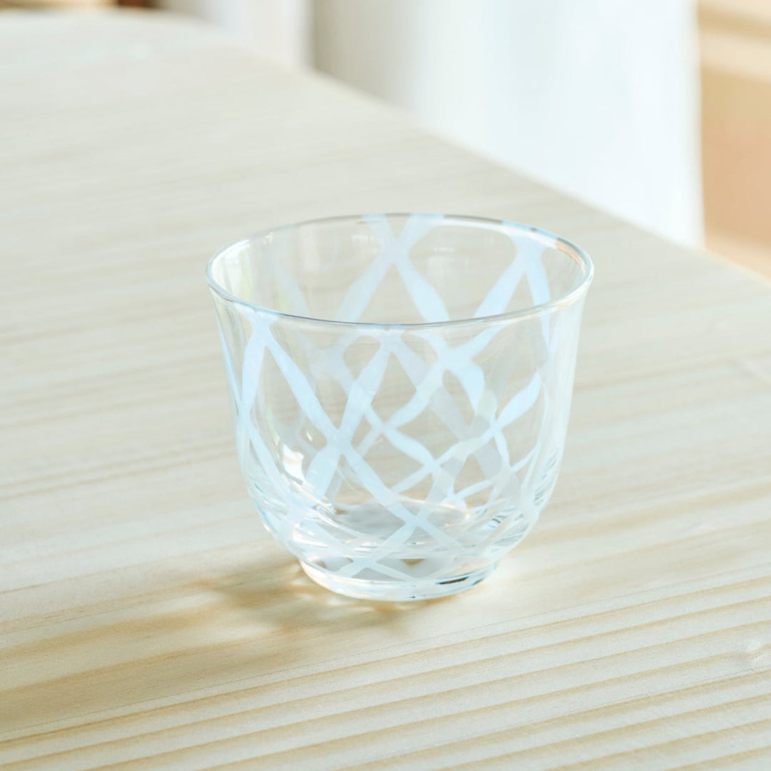 Vintage Japanese glass tea cup with white lattice patterns on a natural wooden table in bright morning sunlight