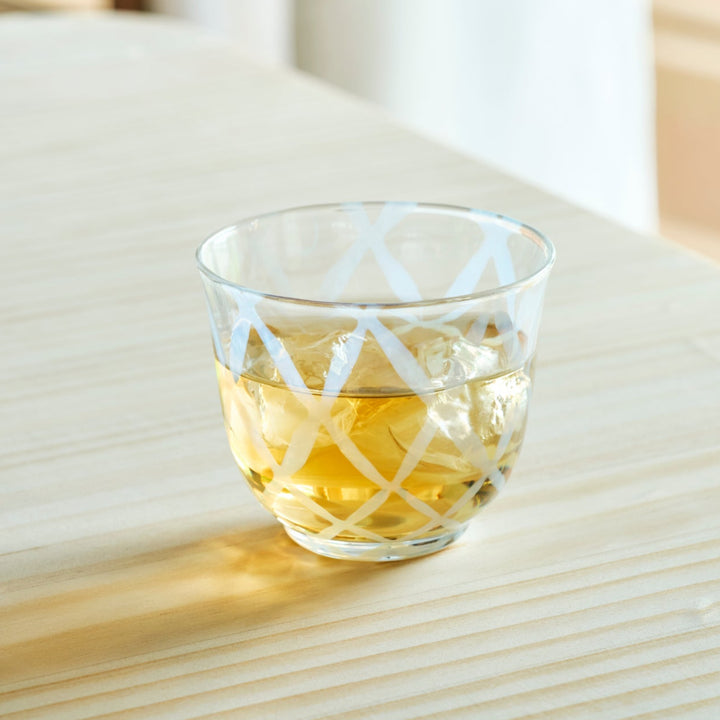 Vintage lattice glass cup filled with iced tea and ice cubes on a wooden table for a refreshing Japanese tea time