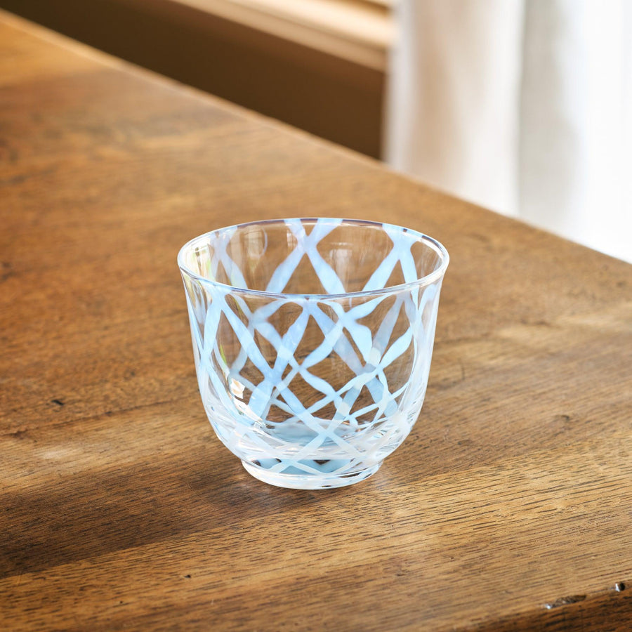 A vintage-style glass tea cup with a light blue lattice pattern, placed on a wooden table in natural light.