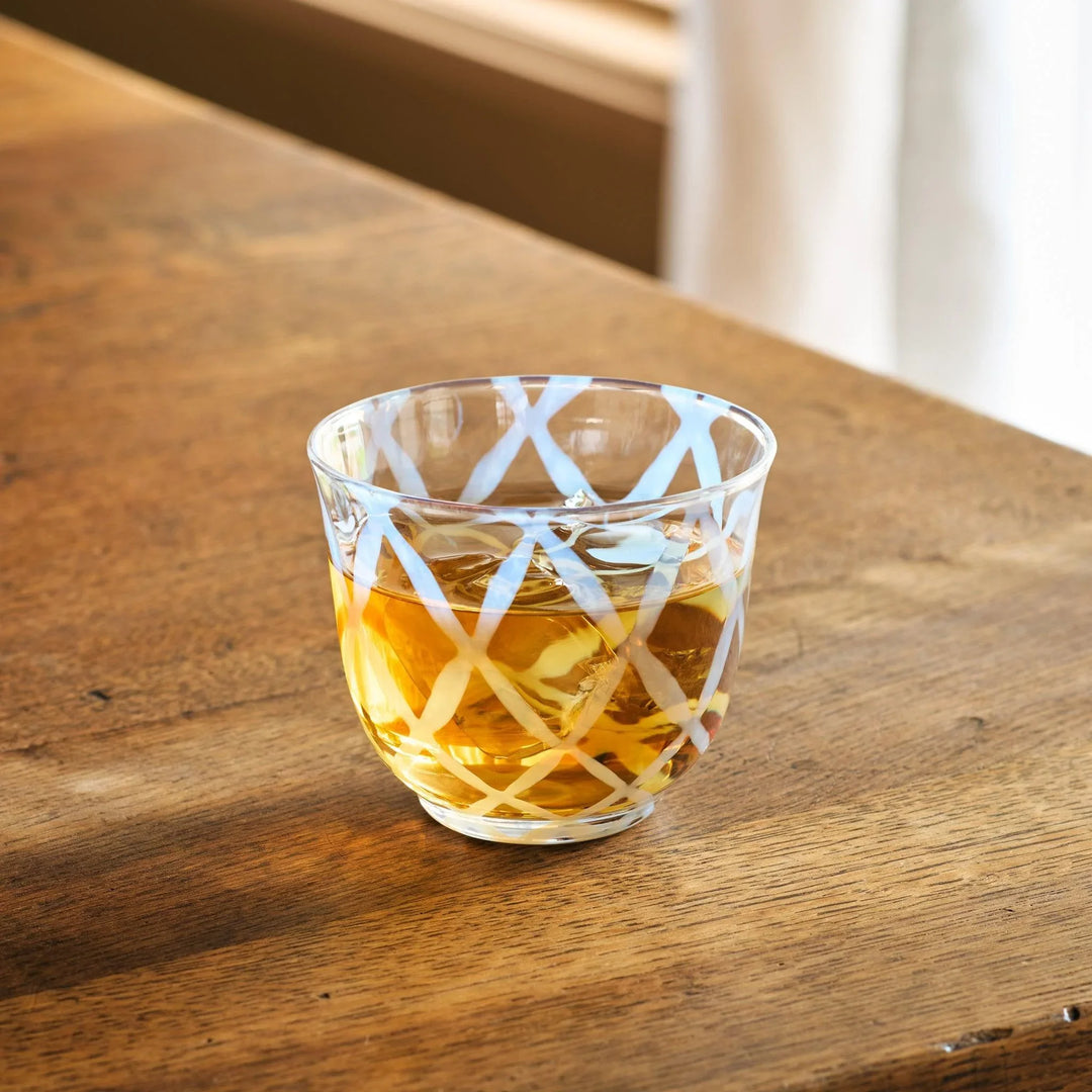 A vintage glass tea cup with a light blue lattice design, filled with amber-colored tea, on a wooden table.