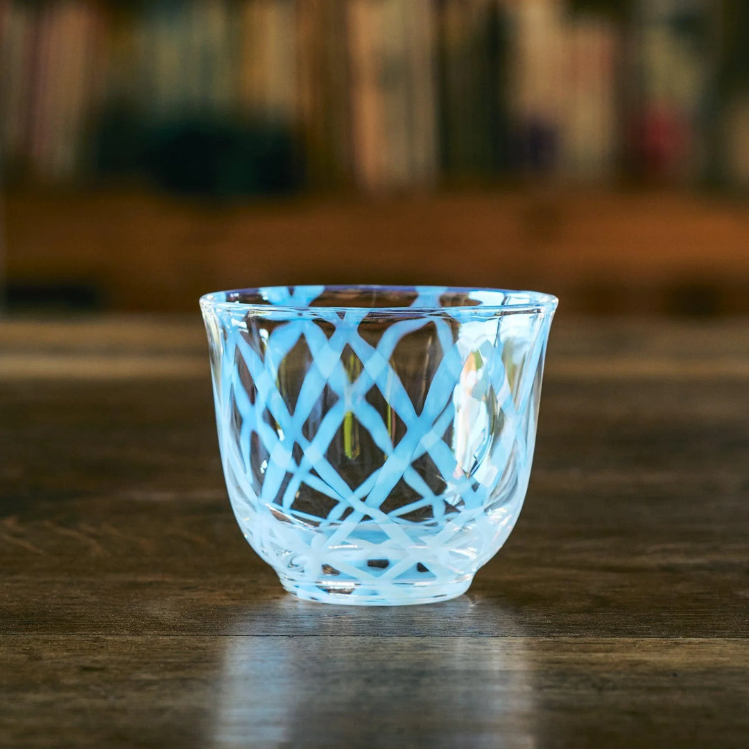 A blue lattice-patterned glass tea cup with gentle curves, displayed on a wooden table in soft light.