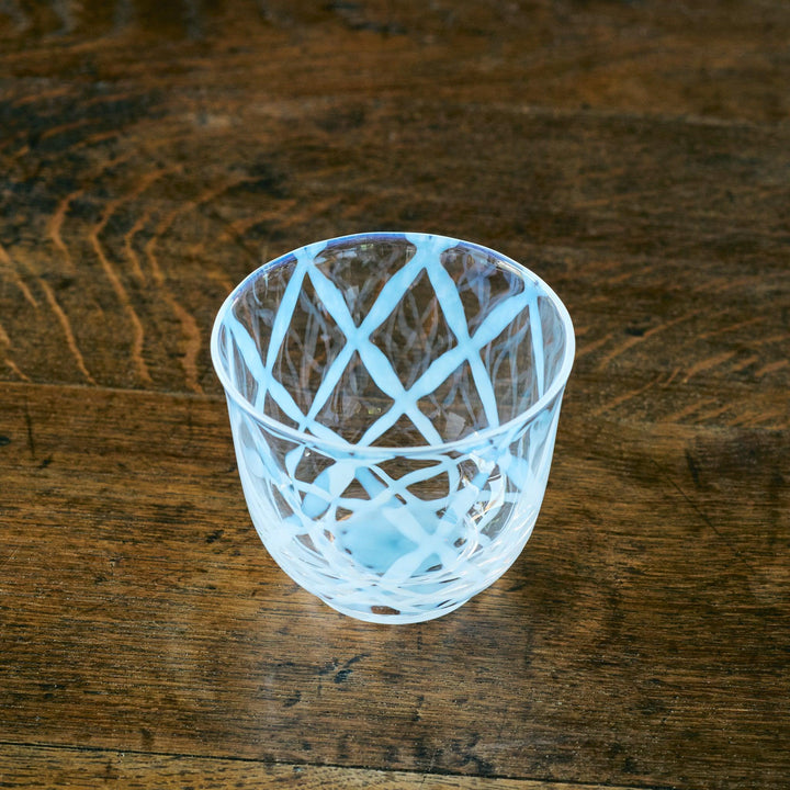 Japanese glass tea cup with intersecting blue lines, viewed from above at an angle on a wooden surface.