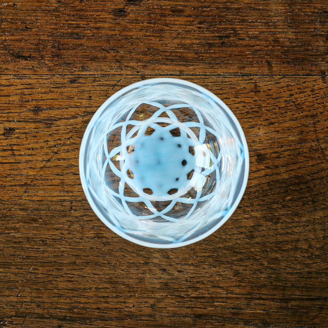 Top view of a glass tea cup with a blue flower-like pattern at the bottom and white lattice designs inside.