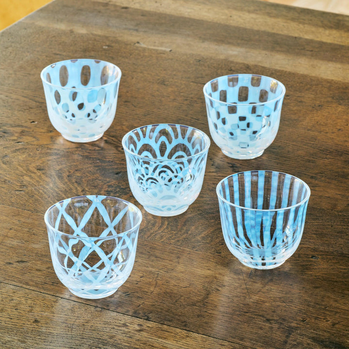 A set of five vintage-style glass tea cups with different blue patterns, arranged on a wooden table.