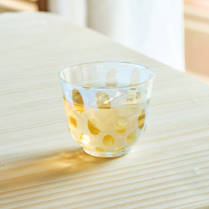 Vintage polka dot glass cup filled with iced tea and ice cubes on a wooden table for a refreshing summer drink