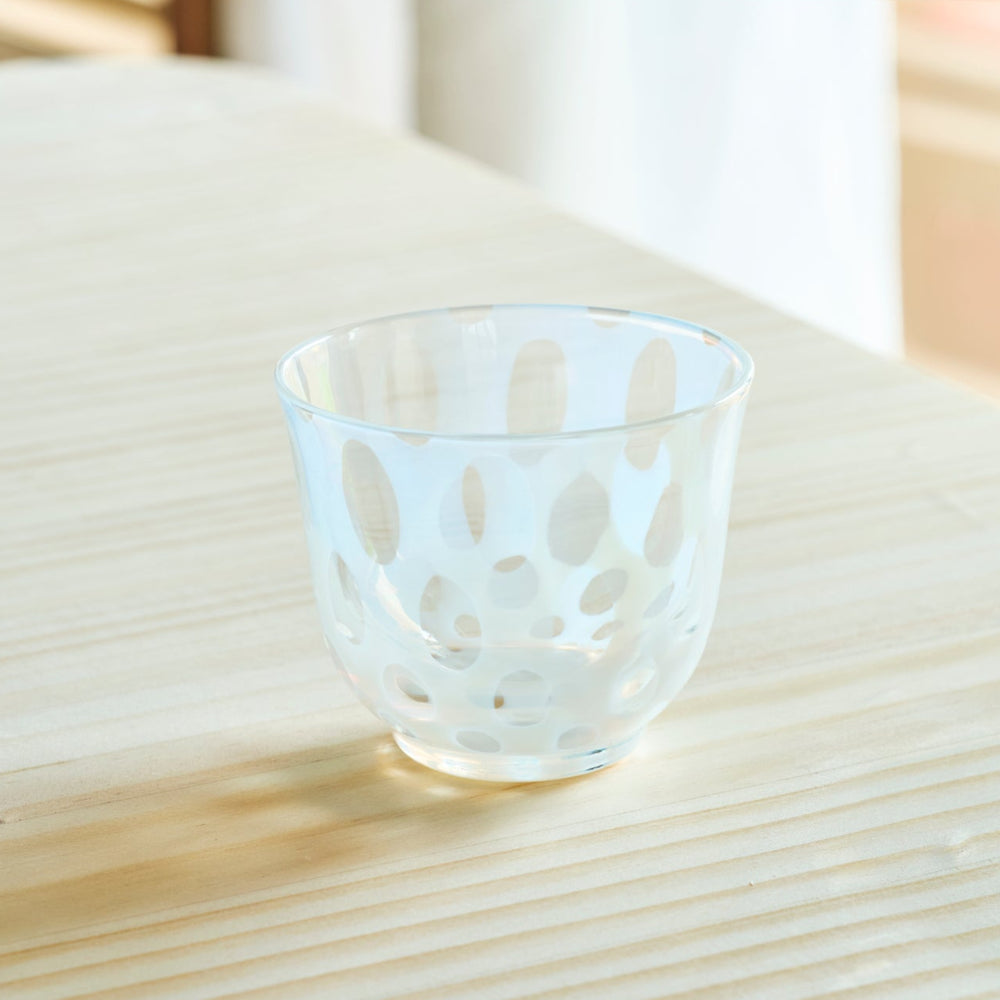 Vintage Japanese glass tea cup with white polka dot patterns on a natural wooden table in bright sunlight