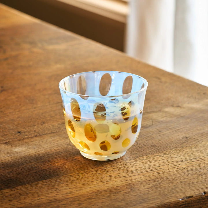 A vintage glass tea cup featuring bold light blue polka dots, set on a wooden table in natural light.