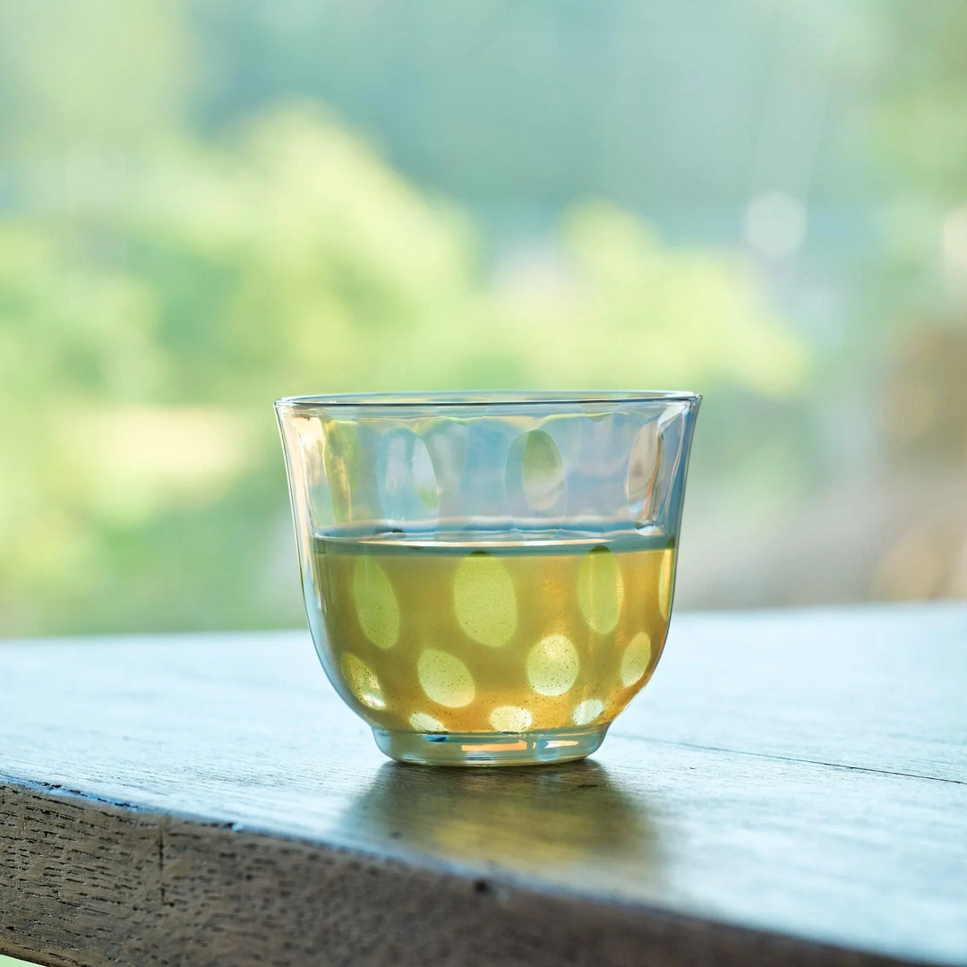 Vintage-style glass cup with translucent dot pattern, filled with green tea by a sunlit window.