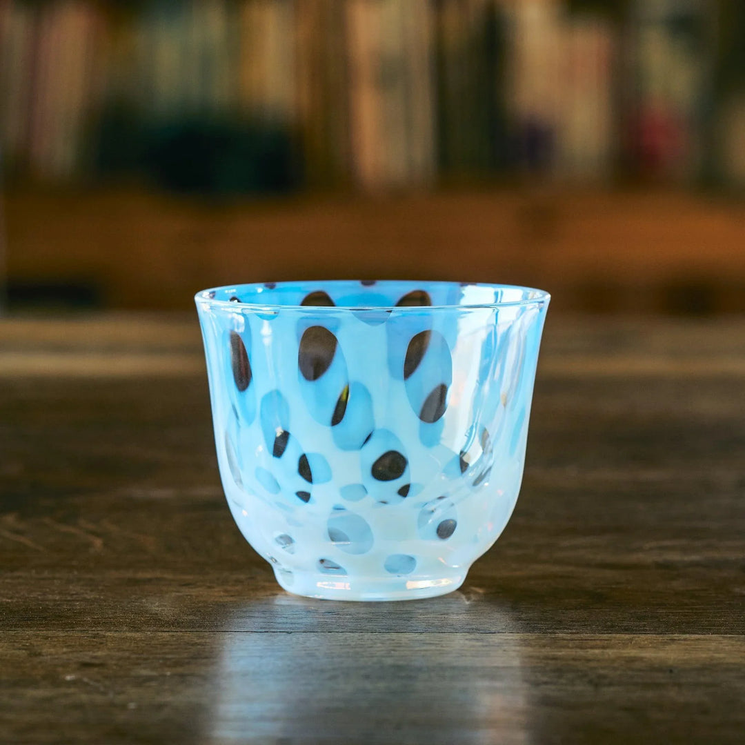 An empty Japanese glass tea cup with playful blue oval dot patterns, resting on a rustic wooden table.
