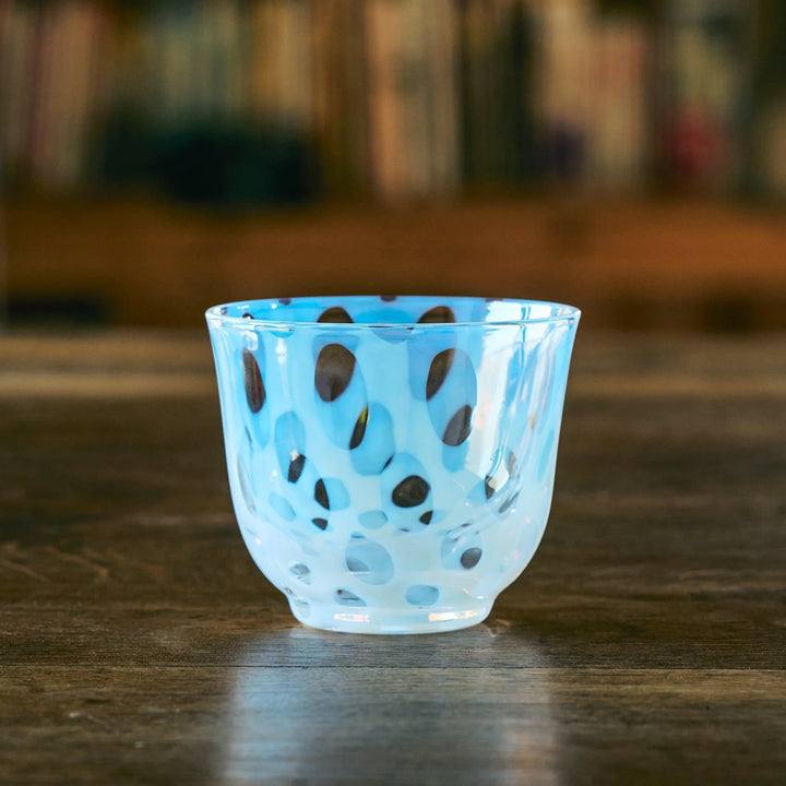 An empty Japanese glass tea cup with playful blue oval dot patterns, resting on a rustic wooden table.