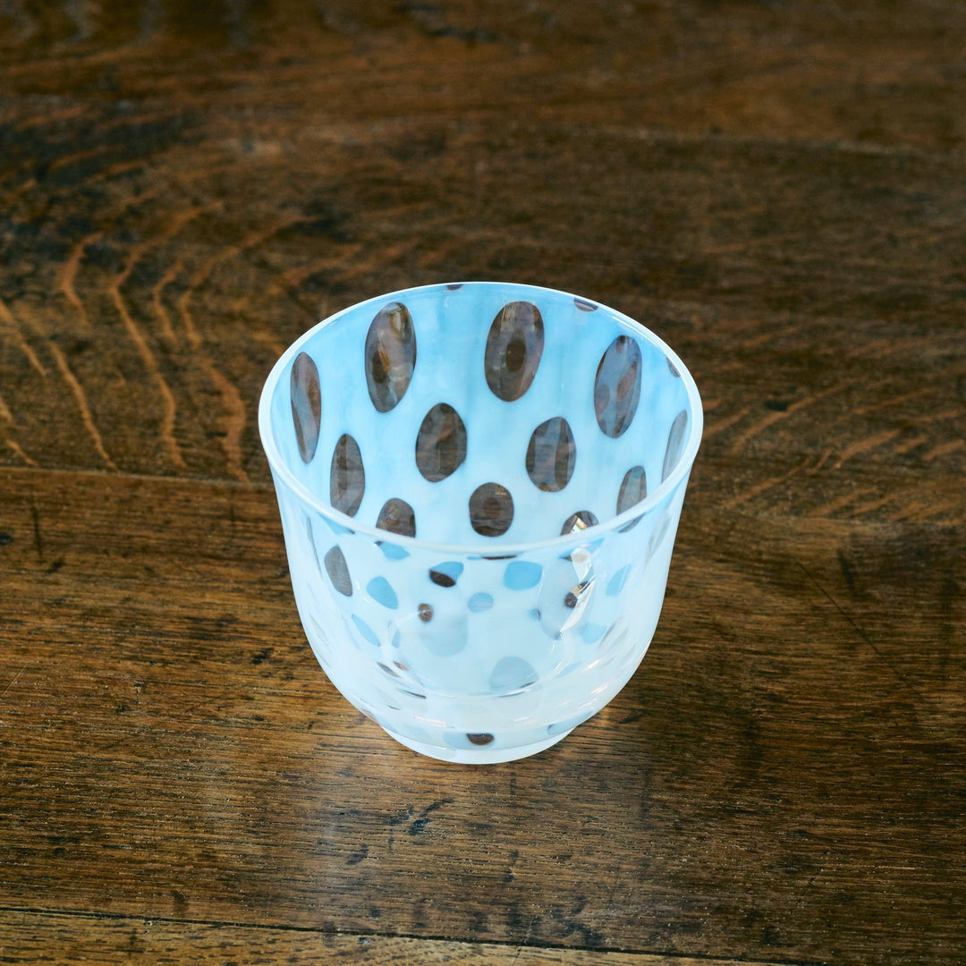 A clear Japanese glass tea cup with pale blue and brown oval dot patterns, viewed from a high angle on wood.