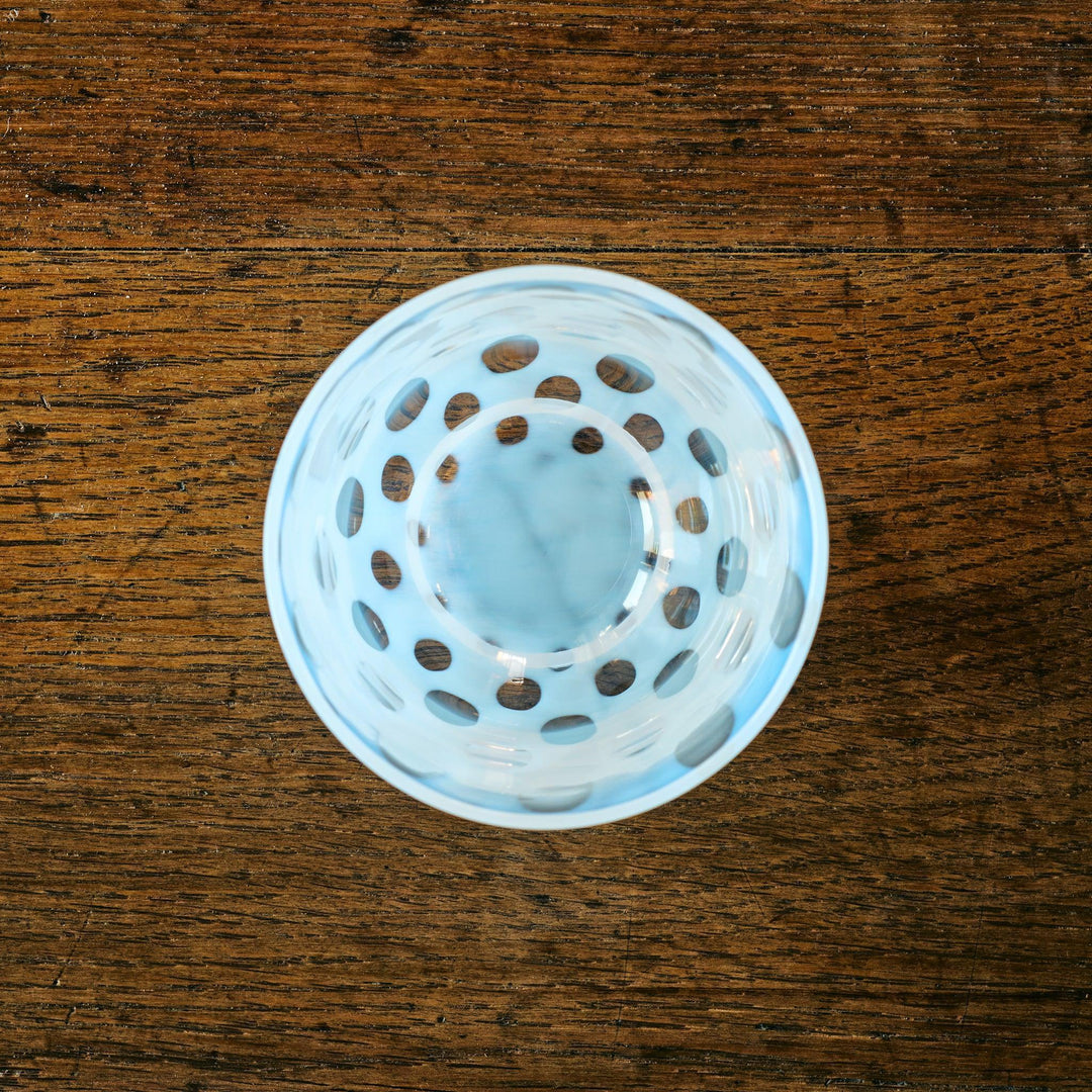 Top-down view of a glass tea cup featuring concentric rings of soft blue dots, resting on a wooden surface.