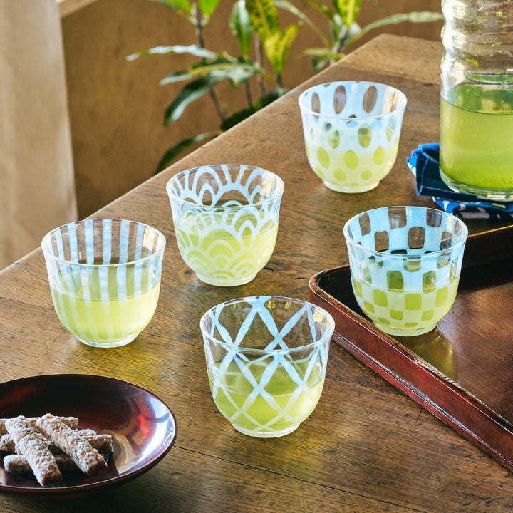 Five patterned glass tea cups filled with green tea, each featuring a unique blue design, set on a wooden table.
