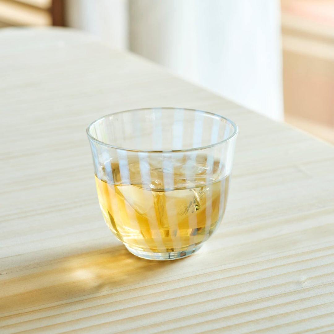 Vintage striped glass tea cup with iced  tea on a natural wooden table in bright morning sunlight