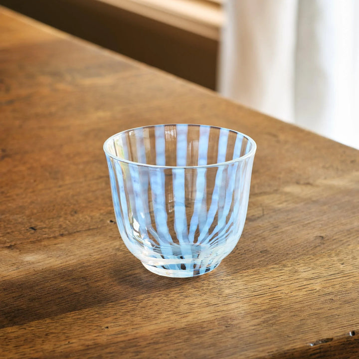 A vintage-style glass tea cup with light blue vertical stripes, placed on a wooden table in natural light.