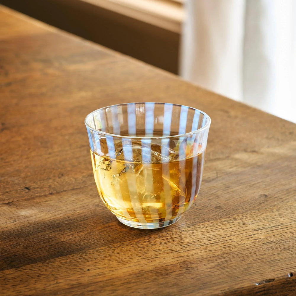A vintage glass tea cup featuring light blue vertical stripes, filled with amber tea and ice, on a wooden table.